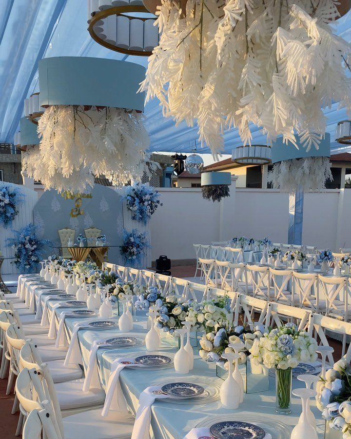 Long wedding reception tables decorated with blue and white flowers under a blue canopy.