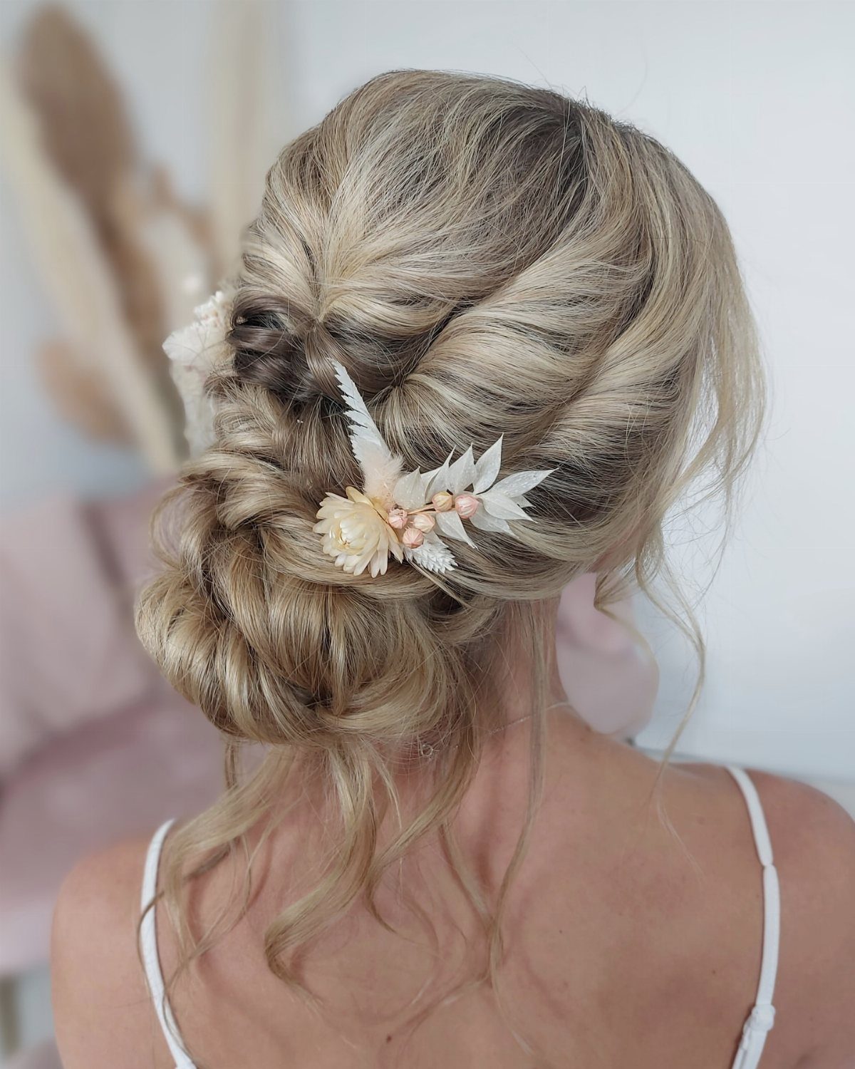 Blonde hair styled in a textured low bun decorated with white dried flowers and pearls.