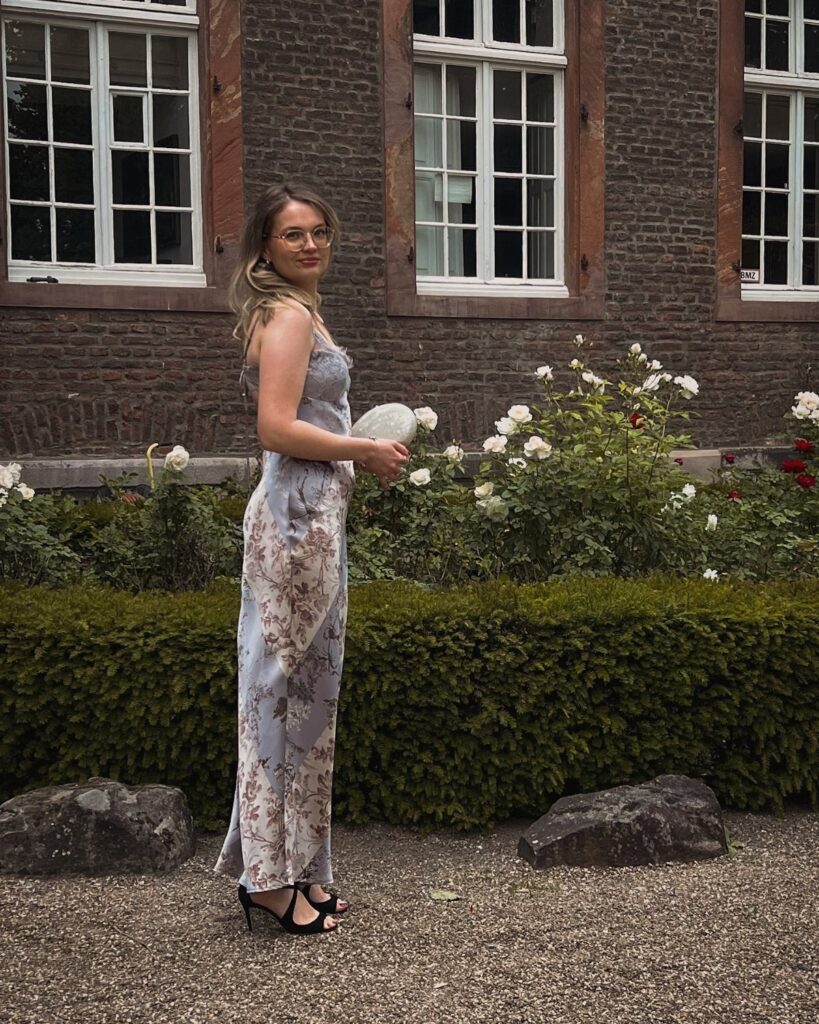 A woman wearing a light blue floral maxi dress and black sandals standing in a garden.