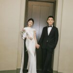 A bride in a white wedding dress and a groom in a tuxedo holding hands.