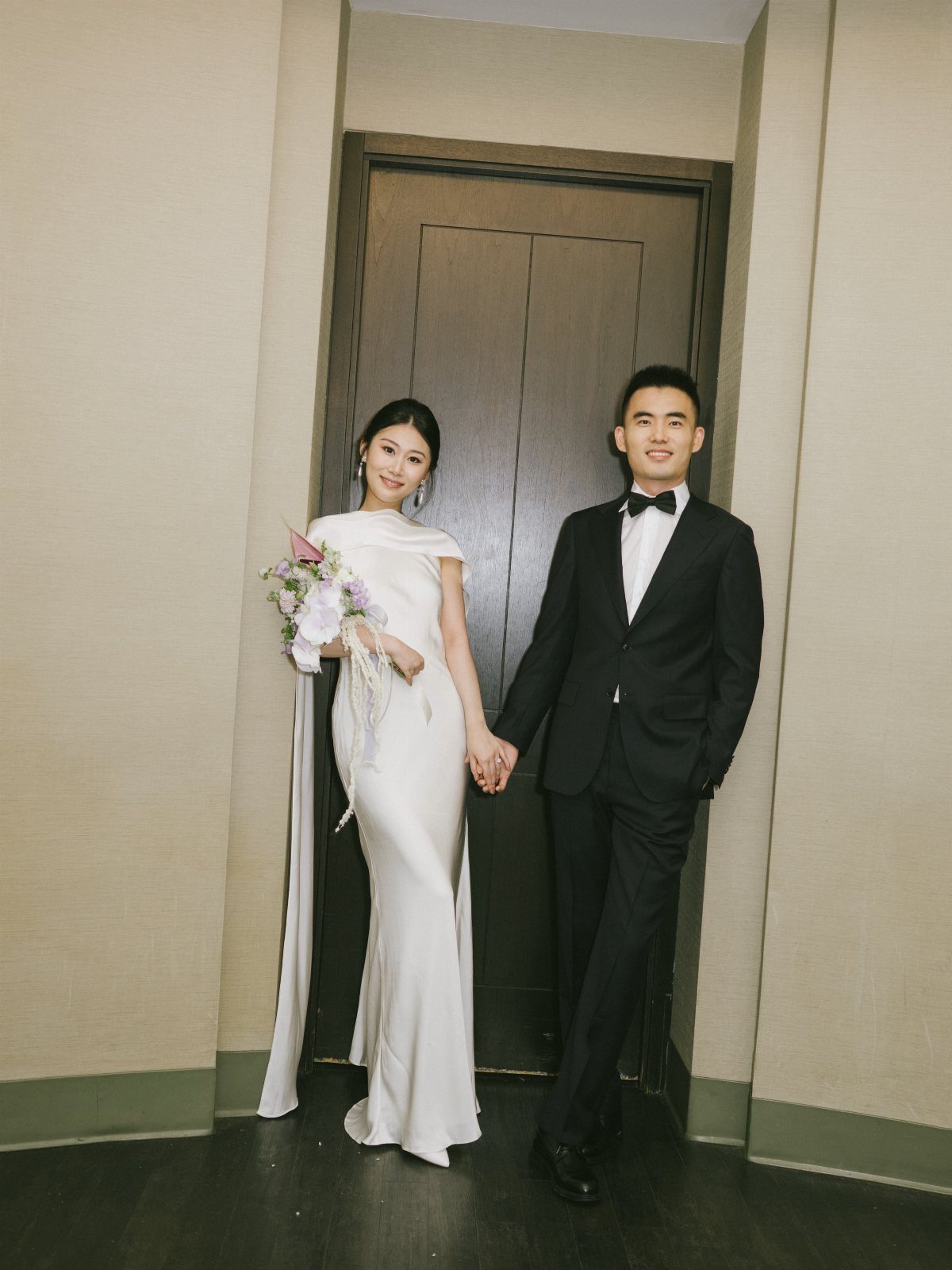 A bride in a white wedding dress and a groom in a tuxedo holding hands.