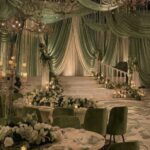 Sage green draped fabric and cream floral arrangements decorate an elegant wedding reception venue.