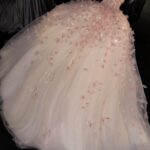 A voluminous light pink tulle wedding dress decorated with floral appliqués and sequins.