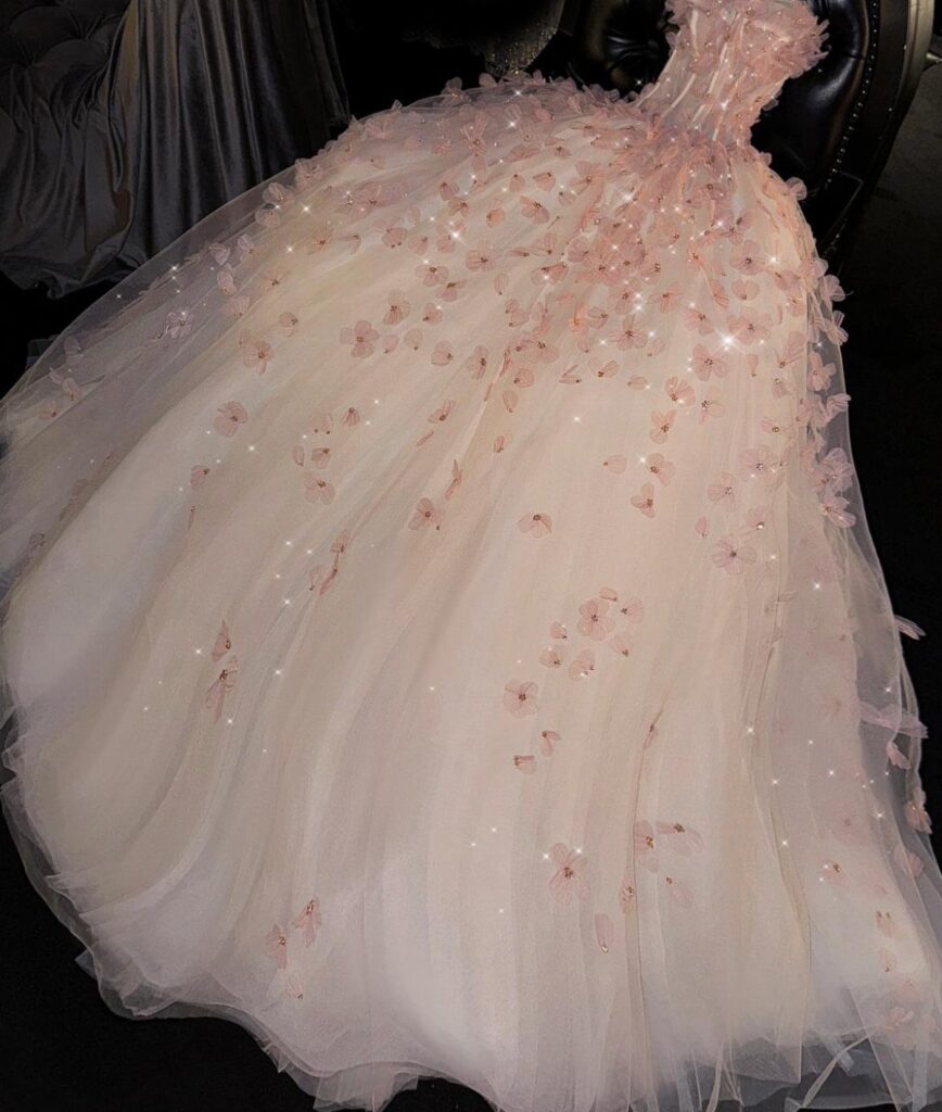 A voluminous light pink tulle wedding dress decorated with floral appliqués and sequins.