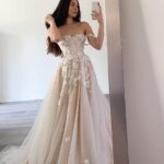 A woman in an off-white lace wedding dress taking a mirror selfie.