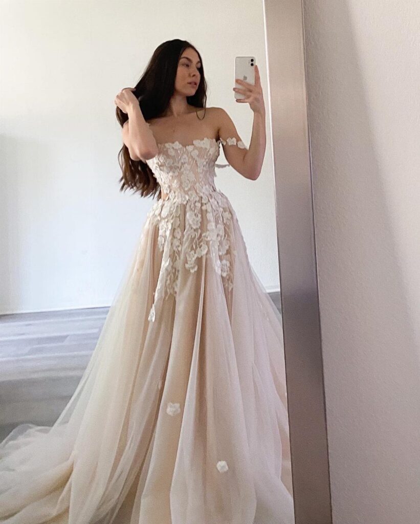 A woman in an off-white lace wedding dress taking a mirror selfie.