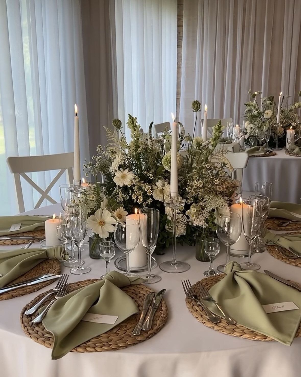 Wedding table setting with olive green napkins, white candles, and a lush floral centerpiece.