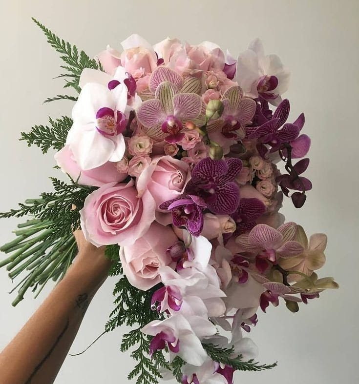 A hand holding a large bouquet of pink roses and various purple and white orchids.