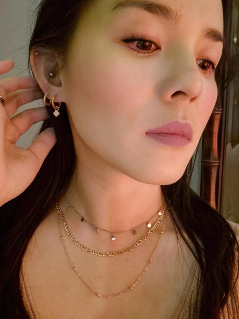 A woman wearing multiple layered gold necklaces and small gold hoop earrings.