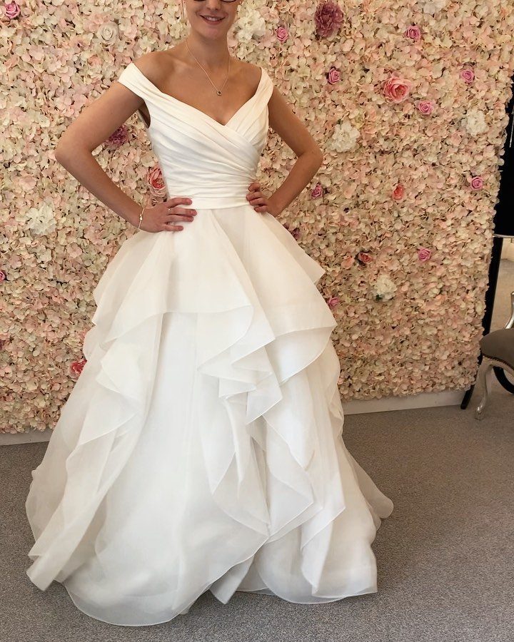 A woman wearing a white wedding dress with a ruffled skirt standing before a floral wall.