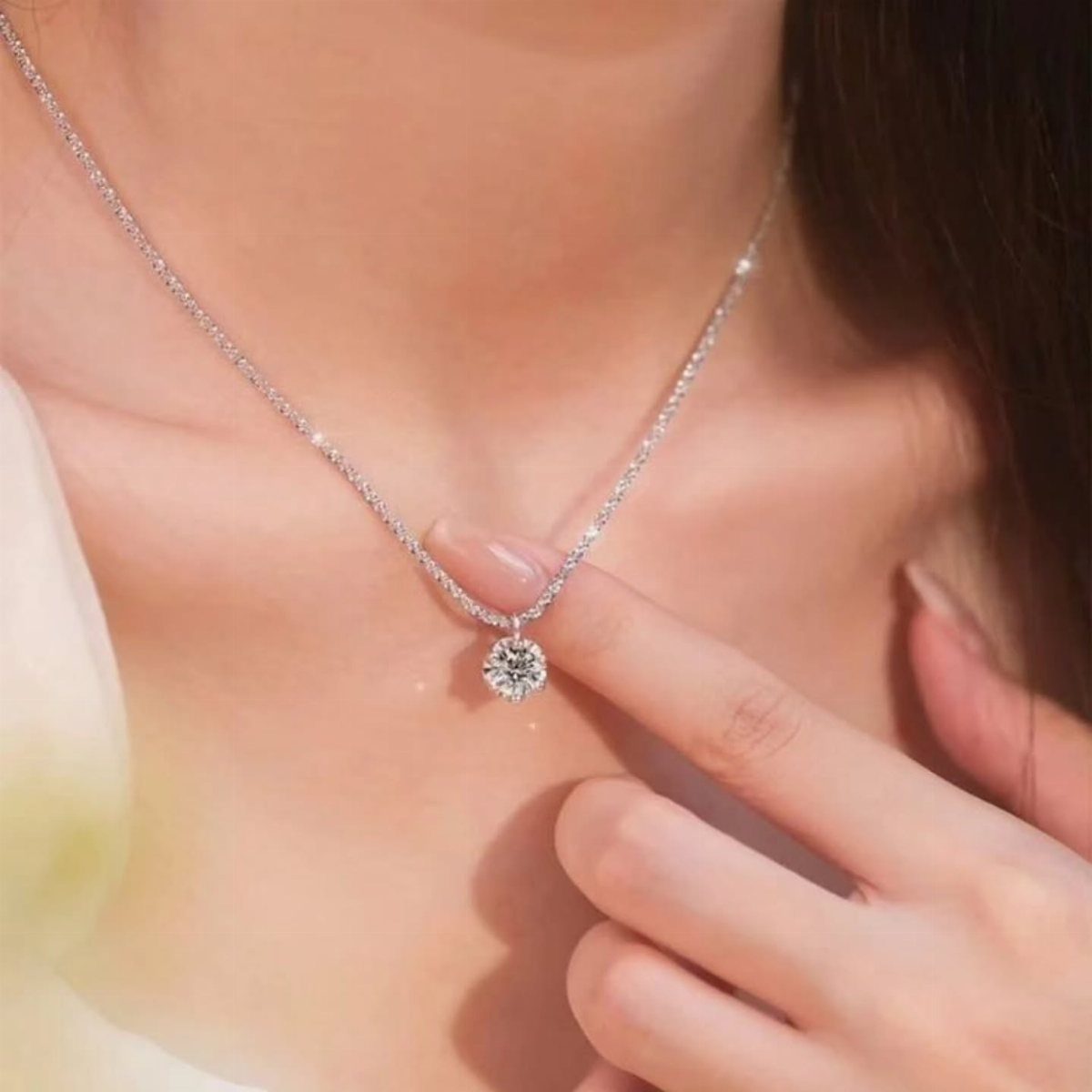 A delicate silver chain necklace featuring a single sparkling round gemstone pendant on a person's neck.