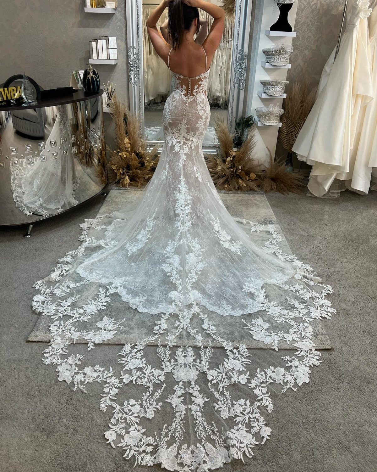 Woman in a white lace wedding dress with a long train standing in a bridal shop.