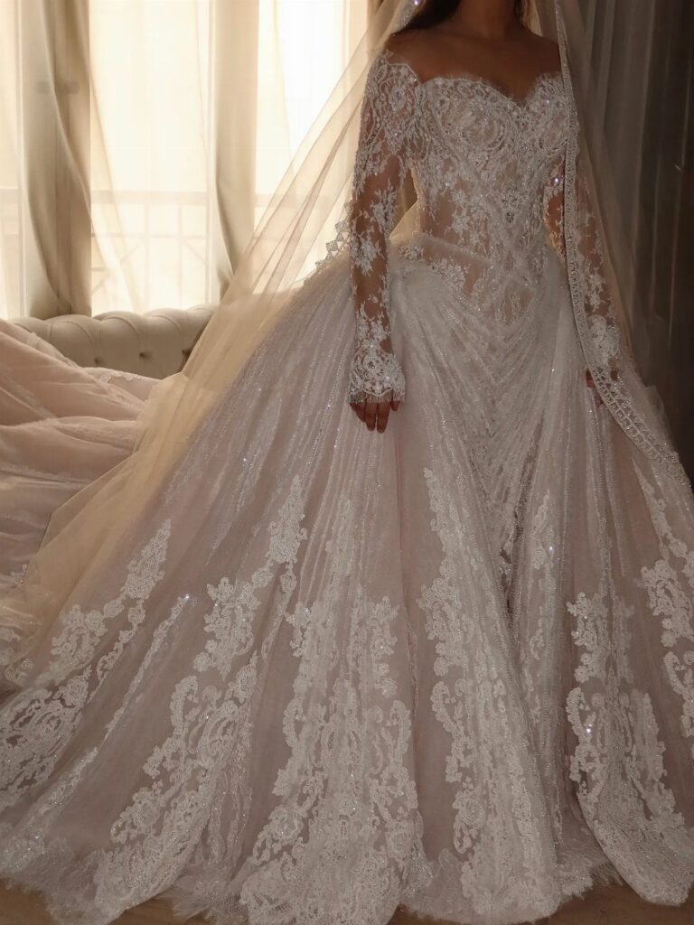 A person wearing a detailed long-sleeved lace wedding dress with a voluminous skirt and veil.