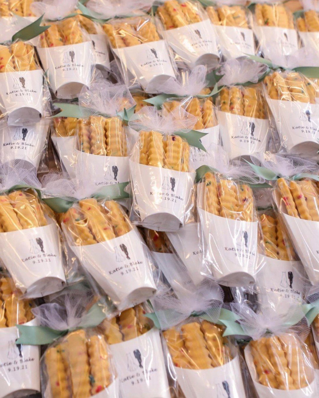 Many small clear bags filled with golden cookies tied with white tulle ribbons.
