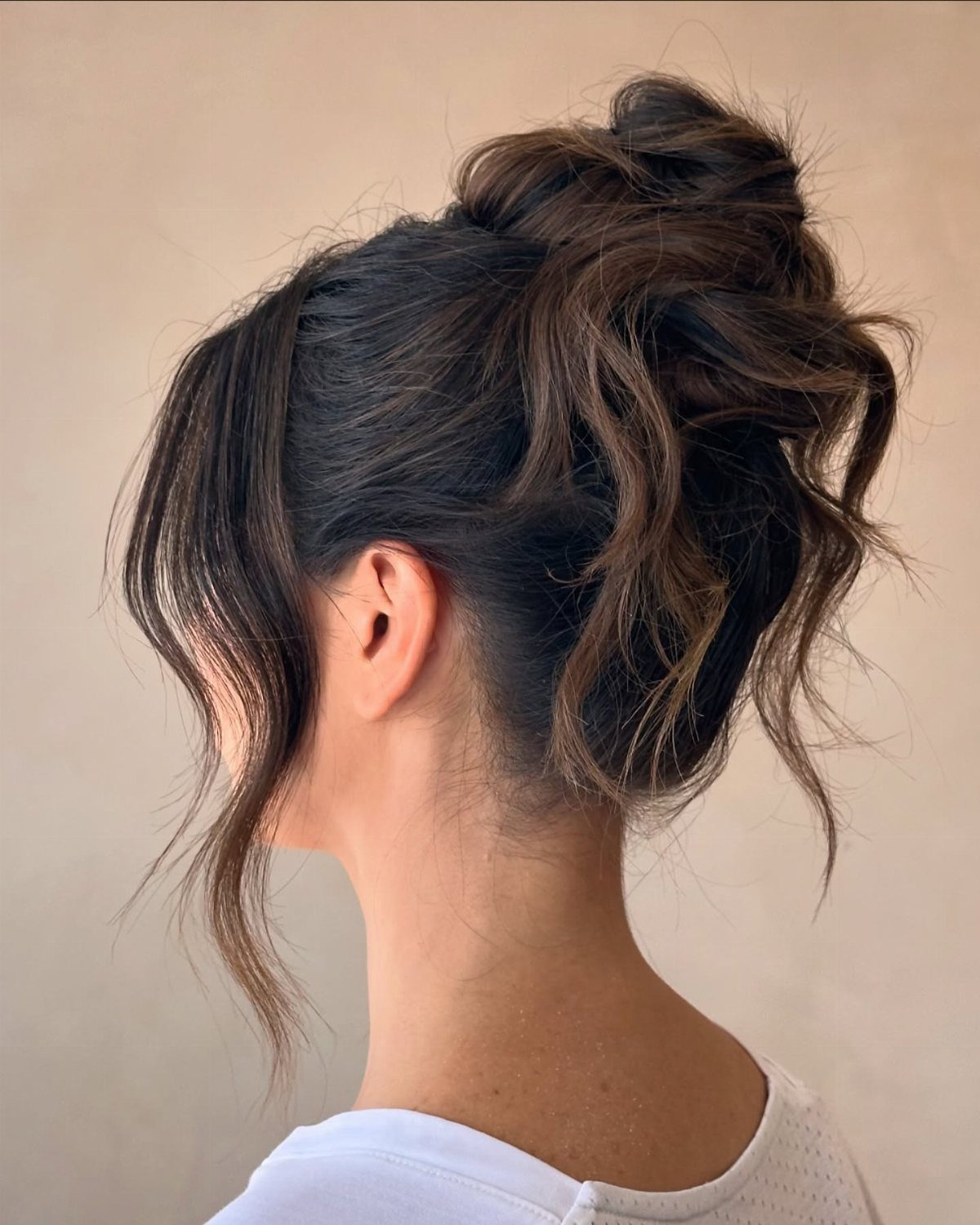 Woman with dark brown hair in a messy, textured updo with loose wavy strands.