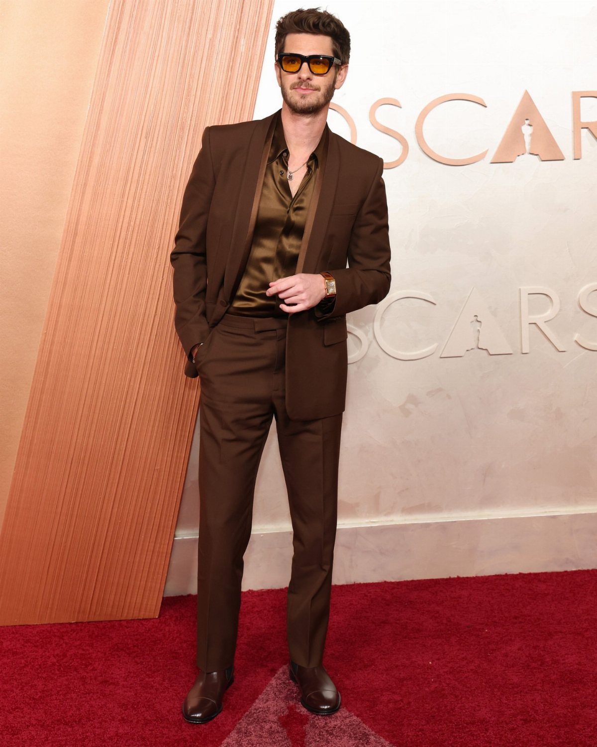 A man in a brown suit and sunglasses posing on a red carpet.