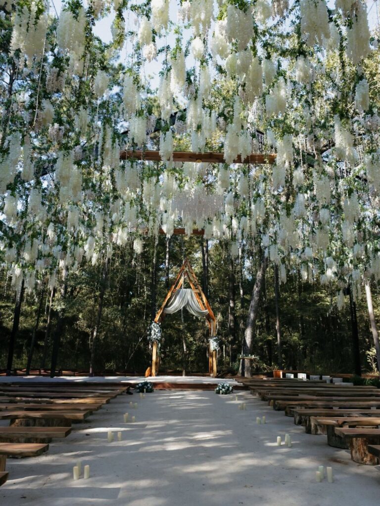 A wedding ceremony setup in a forest with hanging white flowers and a wooden arch.