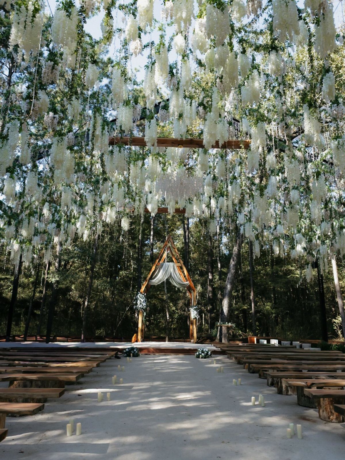 A wedding ceremony setup in a forest with hanging white flowers and a wooden arch.